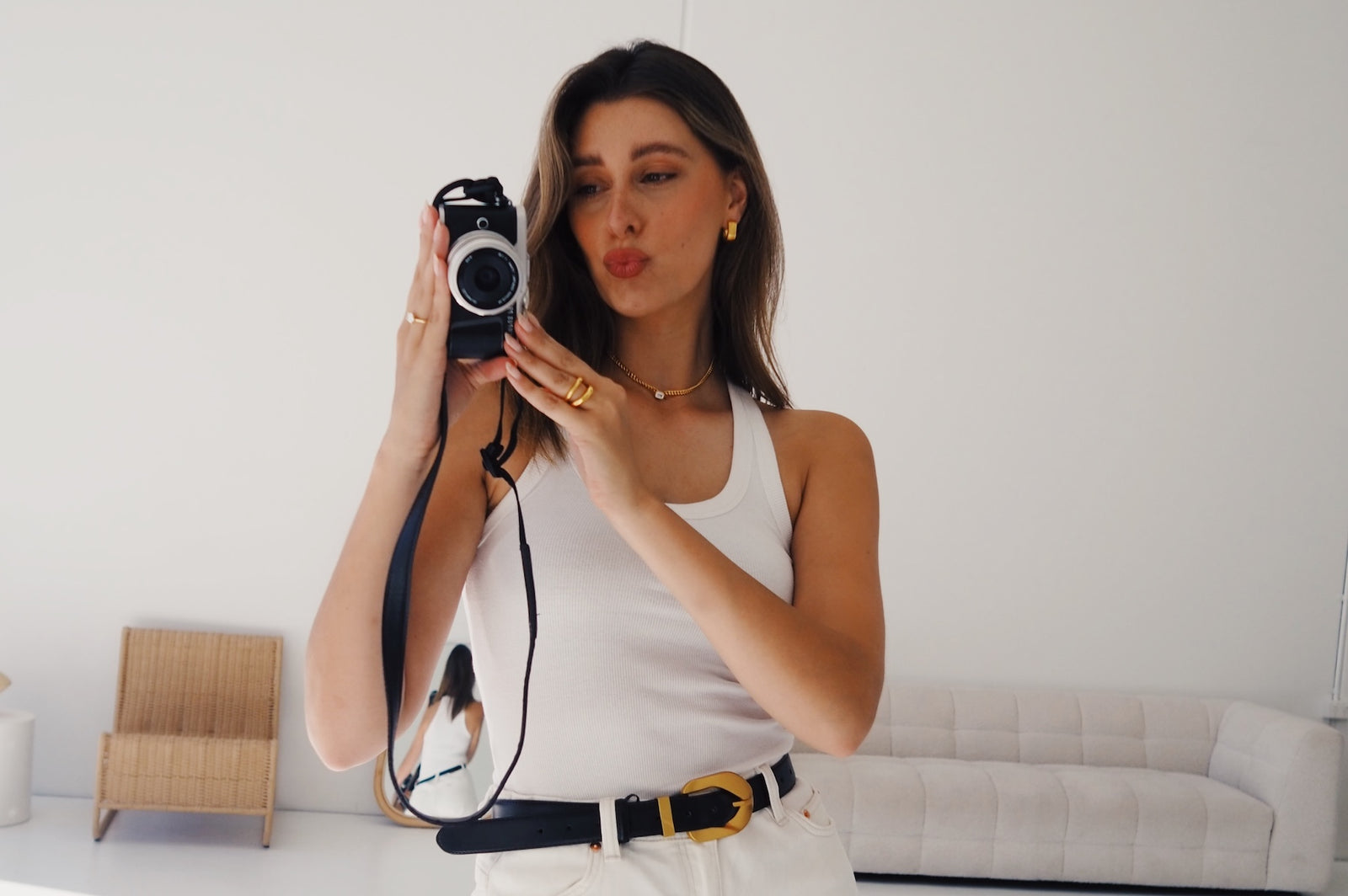 emily nash wearing reliquia jewellery gold earrings necklace and ring, posing with a camera for a selfie